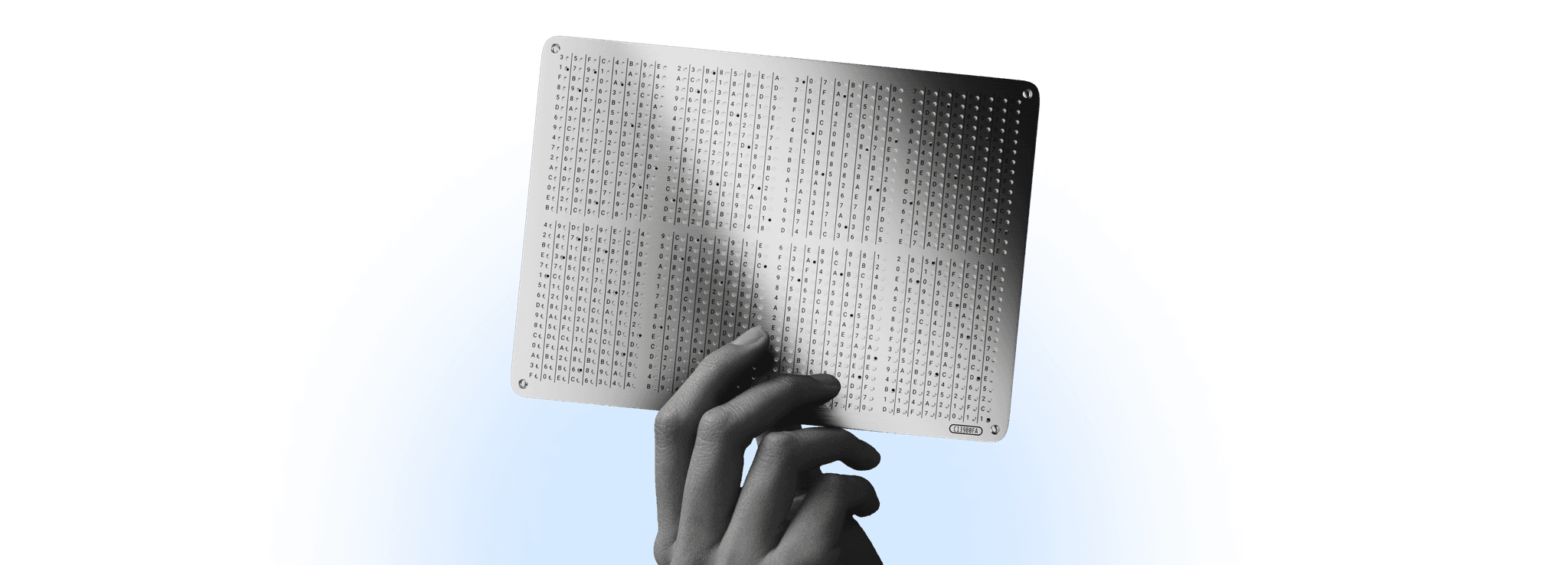 Hand holding up a GRAPHENE steel backup plate engraved with a grid of characters