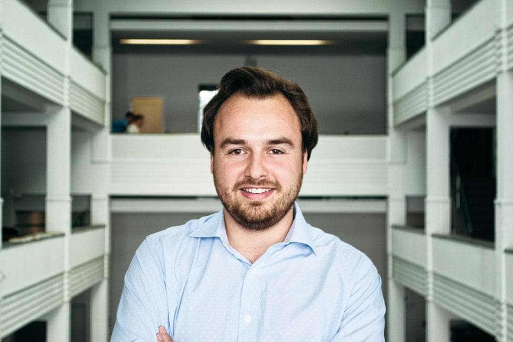 Smiling bearded man in a light blue shirt standing in a white atrium